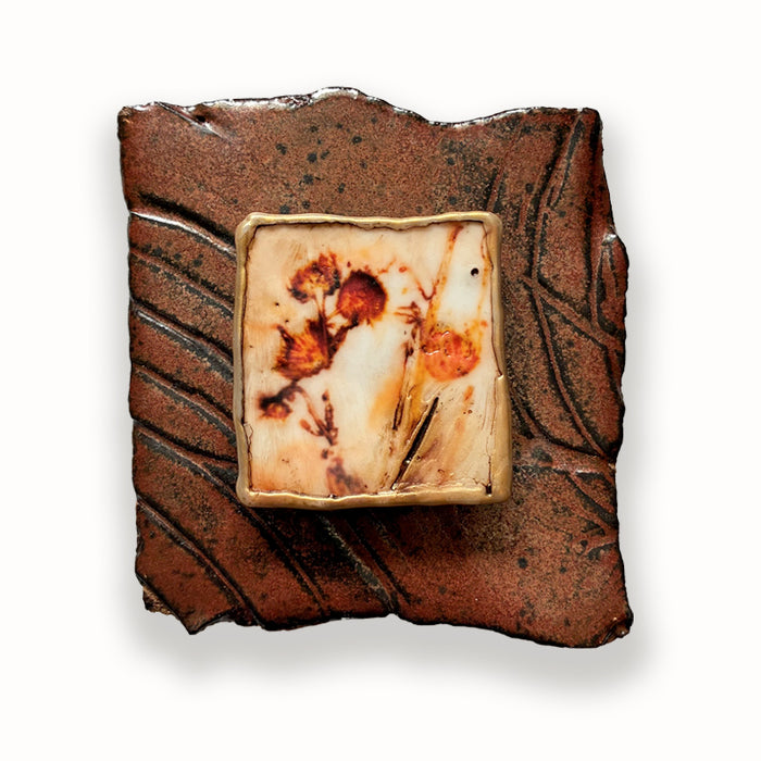 Ceramic tile with irregular shape and texture, with a mixed media orange floral design in the center. Artwork by Sarah Treanor.