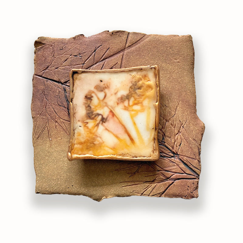 Irregular shaped square ceramic tile with leaf imprints and mixed media, golden floral design in the center. Artwork by Sarah Treanor. 