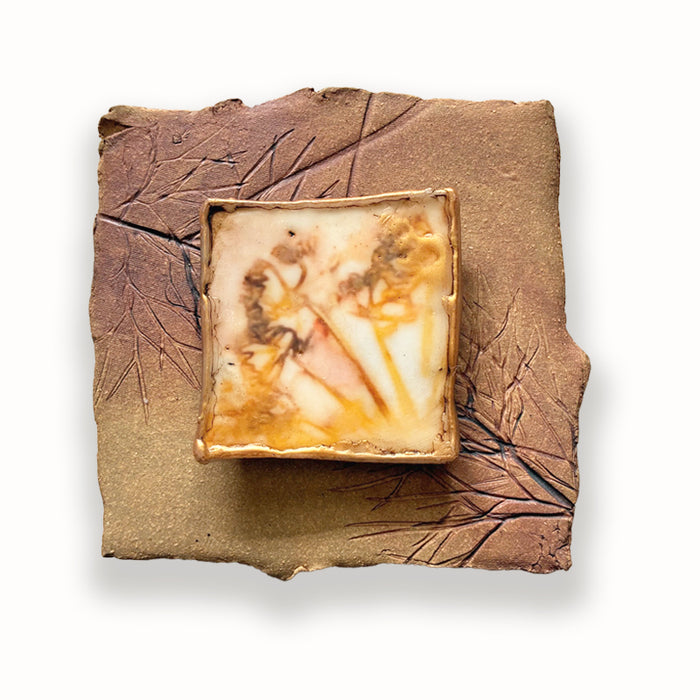 Irregular shaped square ceramic tile with leaf imprints and mixed media, golden floral design in the center. Artwork by Sarah Treanor. 