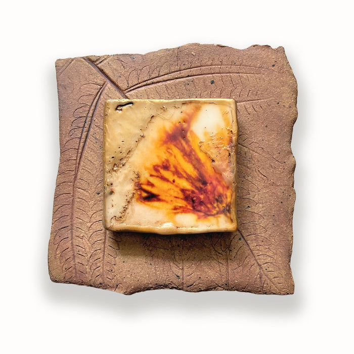 Small ceramic tile wit leaf imprints and mixed media, golden flower design in the center. Artwork by Sarah Treanor.