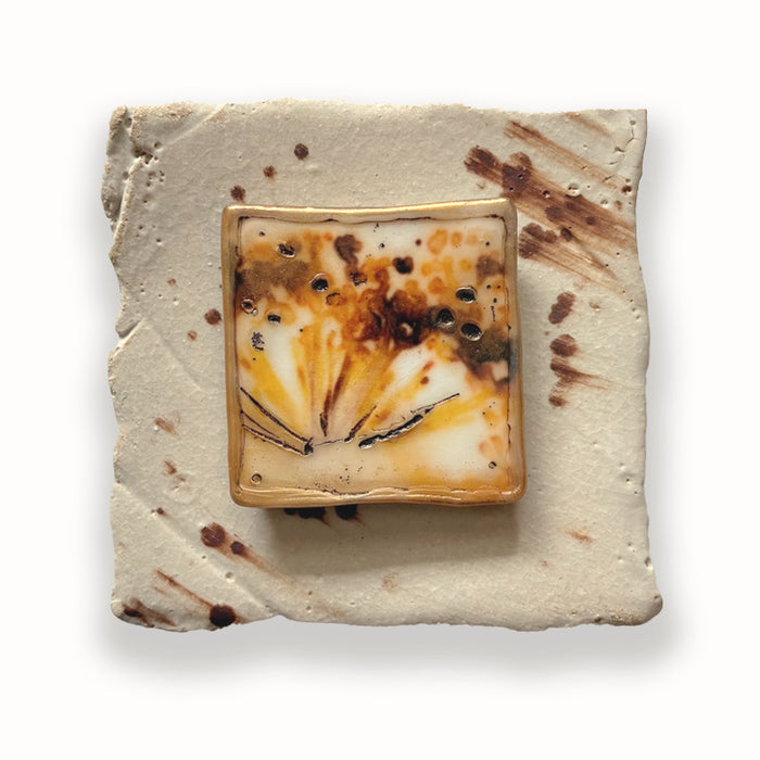 Ceramic tile with a mixed media square center featuring brown and orange flower design. Artwork by Sarah Treanor. 