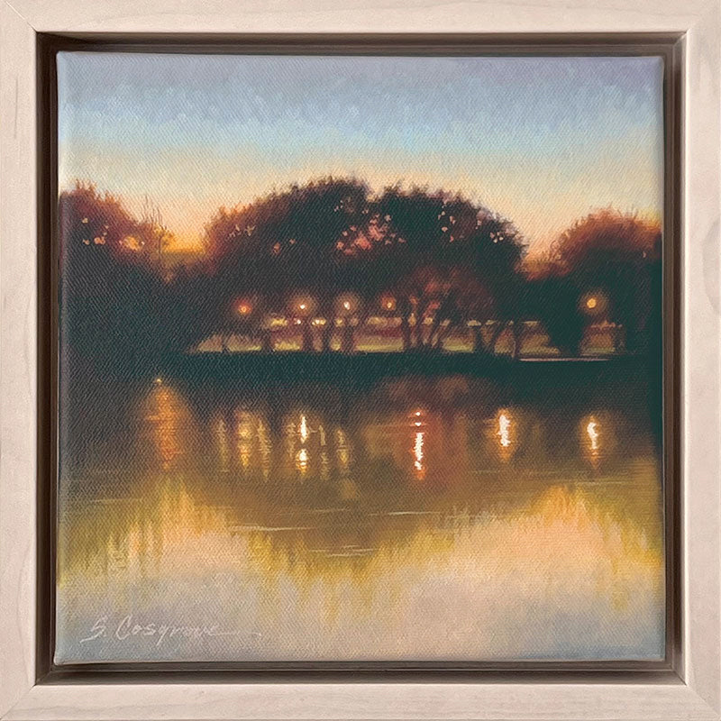 A small landscape painting of a lake at dusk, with silhouetted trees and golden reflections on the water.  The artwork, by Sharon Cosgrove, is set in a hardwood maple frame.