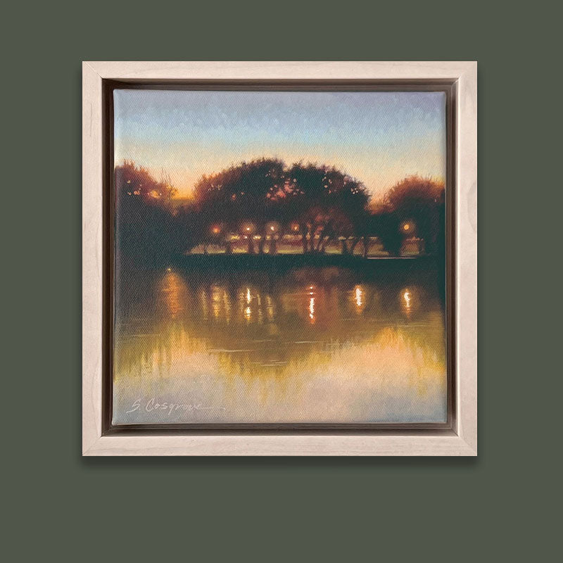 A small landscape painting of a lake at dusk, with silhouetted trees and golden reflections on the water.  The artwork, by Sharon Cosgrove, is set in a hardwood maple frame and displayed on a dark green wall. 
