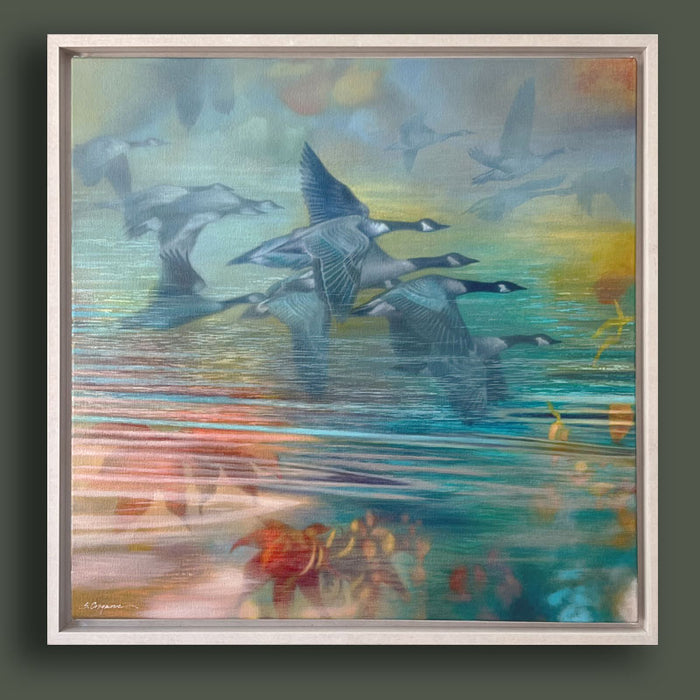 Oil painting with geese flying over reflective water in soft pastel tones of blue, teal, green, yellow, and orange. The artwork, by Sharon Cosgrove, is set in a hardwood maple frame and displayed on dark green wall. 