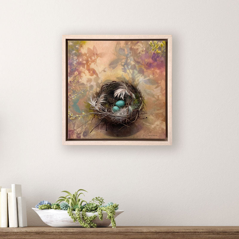Oil painting depicting a bird's nest with two blue eggs, surrounded by soft botanical. Artwork by Sharon Cosgrove, set in a maple hardwood frame and displayed over a table. 