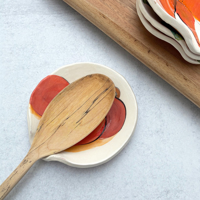 Handmade ceramic spoon rest with apple decoration by artist Molly Lithgo. Image shows wooden spoon resting on spoon rest.
