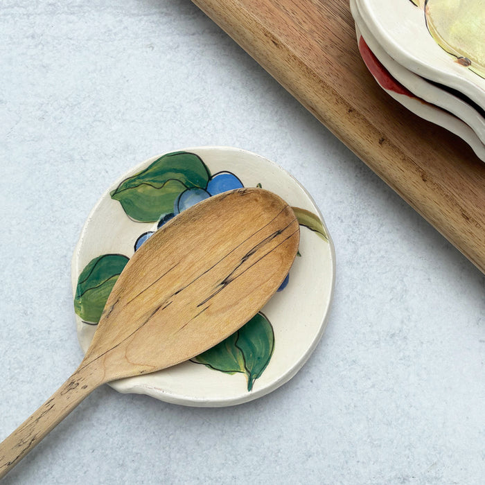Handmade ceramic spoon rest with apple decoration by artist Molly Lithgo. Image shows wooden spoon on spoon rest. 