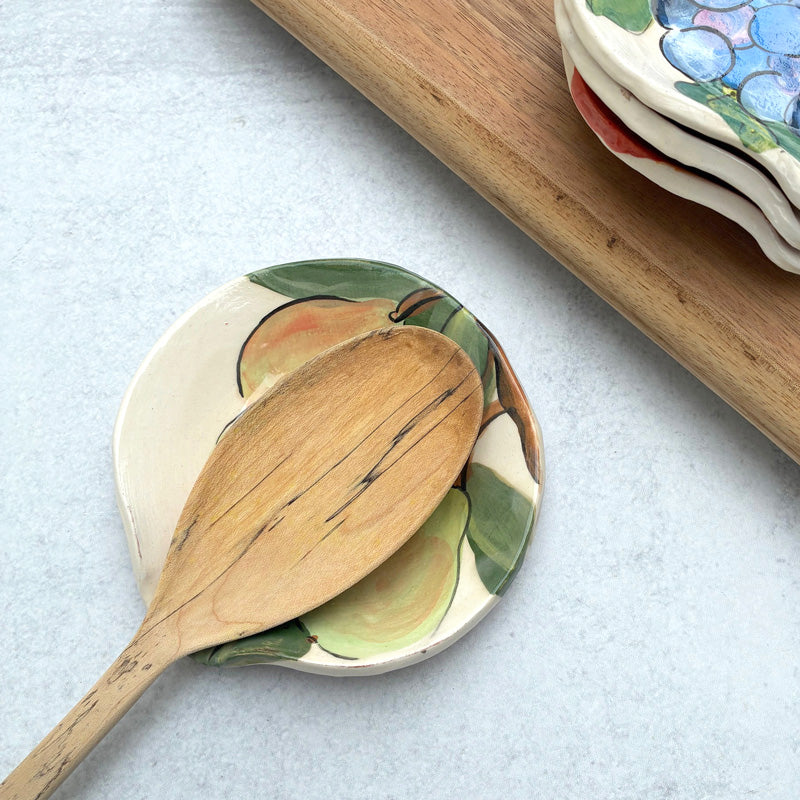 Handmade ceramic spoon rest with pear decoration by artist Molly Lithgo. Image shows wooden spoon on spoon rest. 