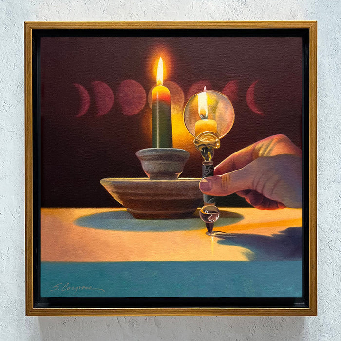 Framed painting by Sharon Cosgrove of a hand holding a magnifying glass in front of a candle, creating a second candle flame, with the moon phases in the background. Shown hanging on wall. 