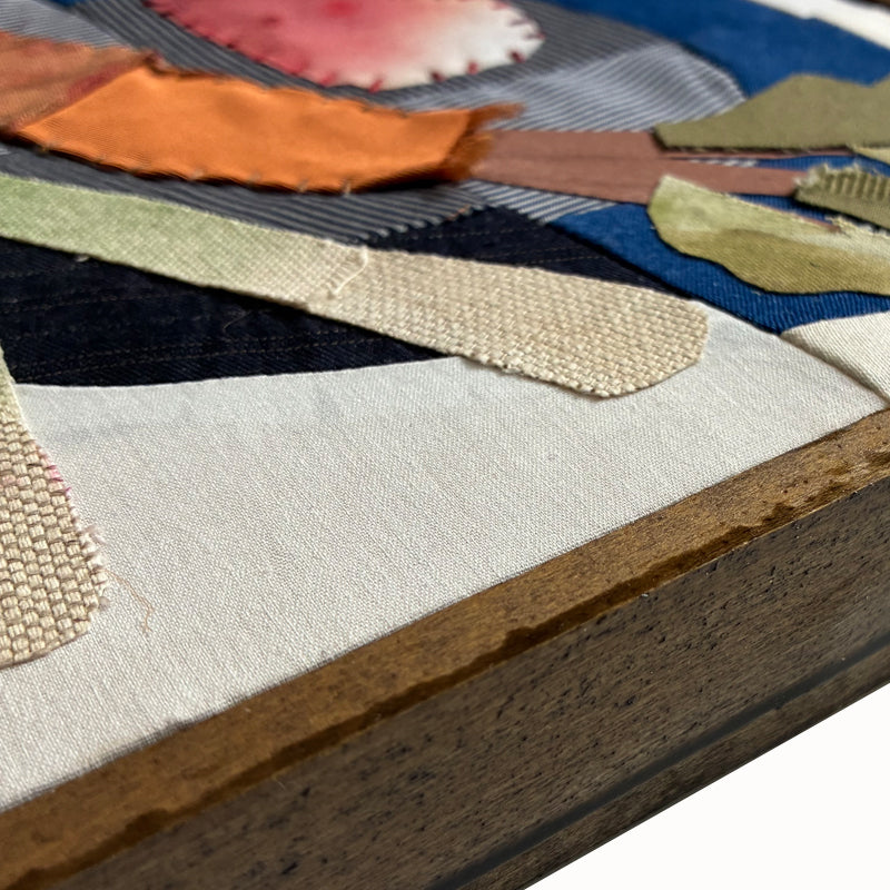 Veggie Plate textile collage by artist Hannah Goff. The artwork is comprised of hand-sewn and painted, reclaimed and recycled fabrics. It features a carrot, radishes and green onions on a blue plate. Finished in a handmade rustic wood frame. Close up detail, side view.